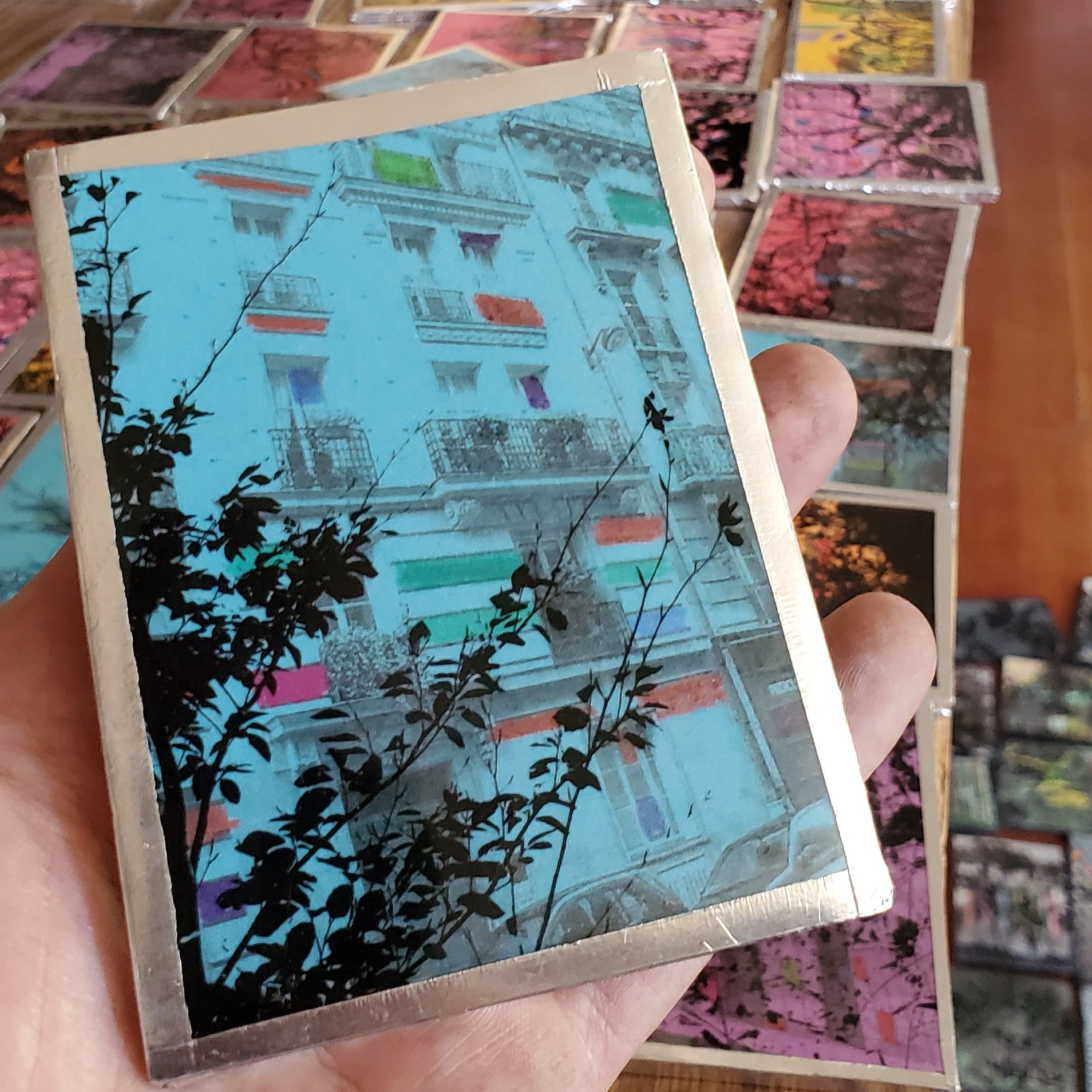 Hand holding a small, colorful paper model of a building with a tree in front.
