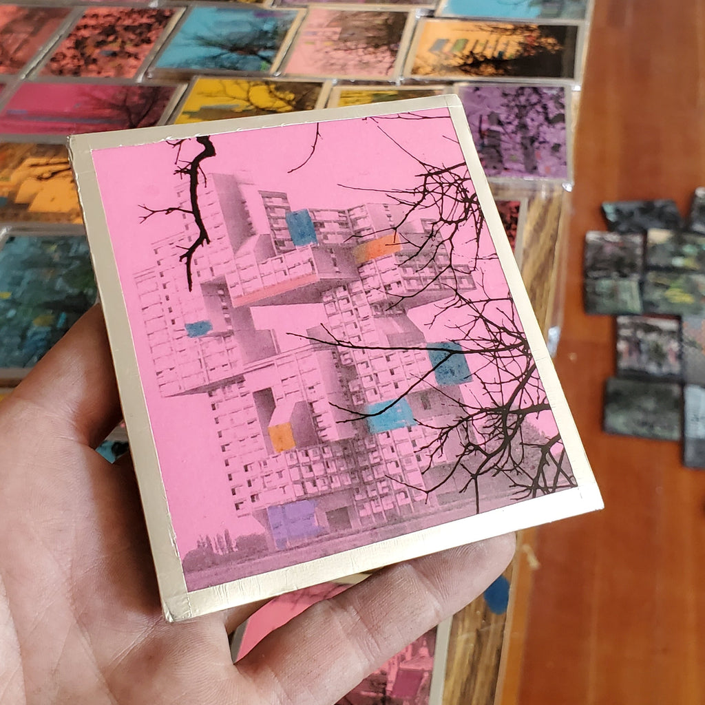 Hand holding a small pink notebook with tree design, surrounded by more notebooks in a store setting.